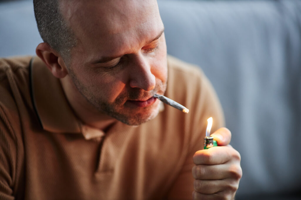 Adult man lighting up weed cigarette smoking at home. Marijuana and Mental Health: The Psychosis connection