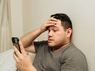 Hispanic male using the smartphone, putting his hand on his head, looking worried